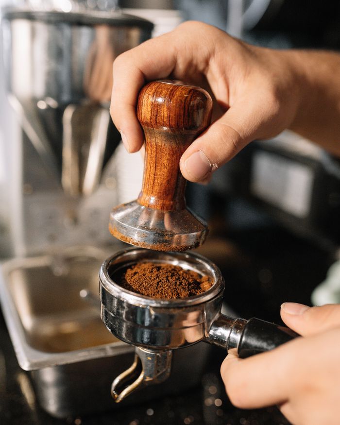A barista using a tamper to prepare ground coffee in a portafilter, perfect for espresso enthusiasts.