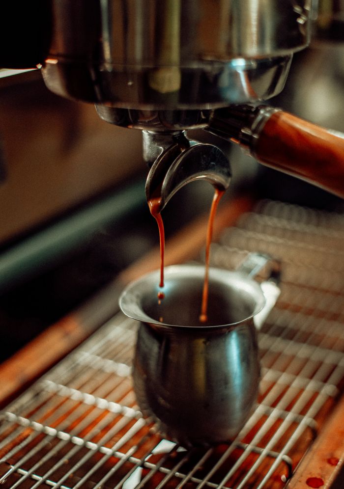 Close-up of espresso pouring from a machine into a metal cup in a Baku coffee shop.