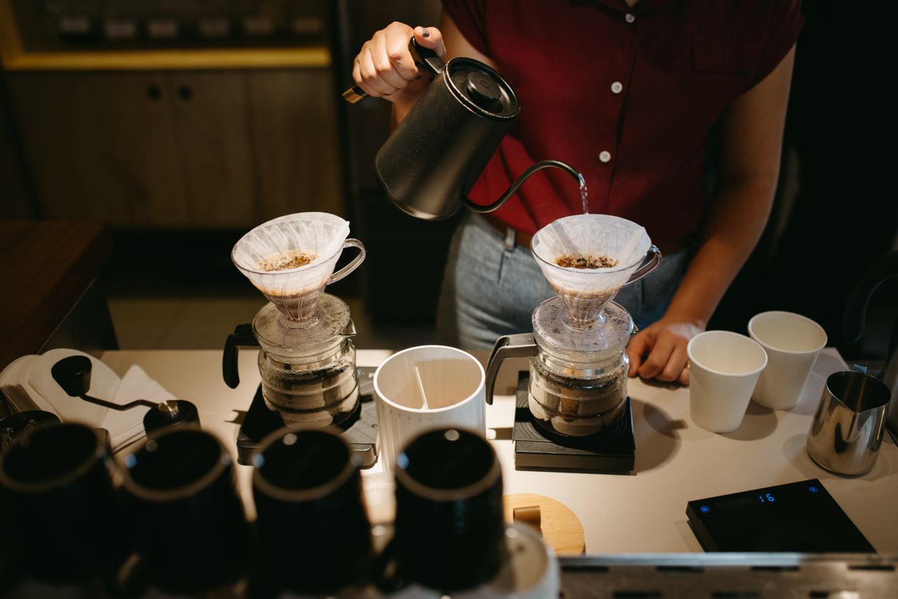 Barista hand-pours coffee using a drip method, showcasing modern coffee culture.