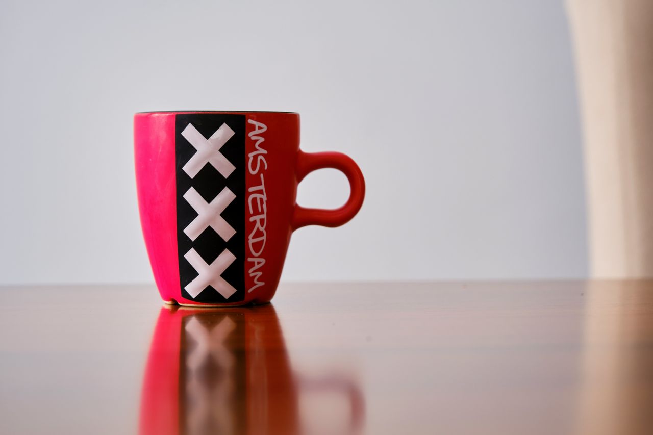 Red mug with Amsterdam's iconic XXX design on a reflective surface.
