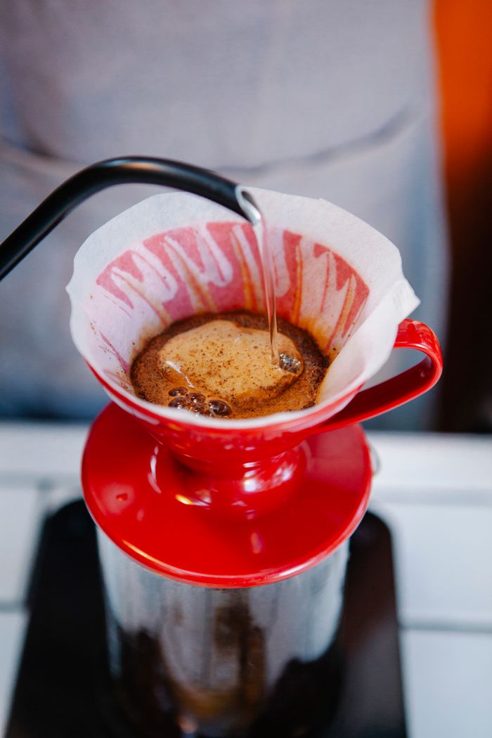 From above of hot coffee brewing with barista pouring hot water form kettle